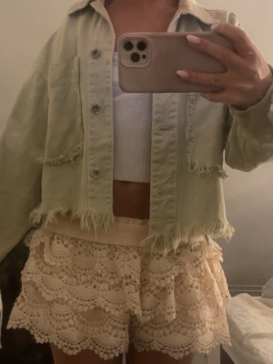 Grön jeansjacka - Trendig grön croppad jeansjacka med råa, fransiga kanter och stora fickor framtill. Jackan har knappstängning och en avslappnad passform som ger en cool och avslappnad vibe. Perfekt för dig som vill sticka ut med en unik jeansjacka.
