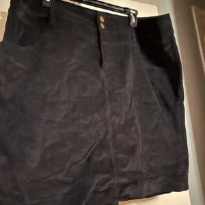 Svart manchesterkjol från bpc - Snygg svart kjol i manchester från bpc. Kjolen har två framfickor, knapp- och dragkedjestängning framtill och en klassisk rak passform. Perfekt för dig som gillar en enkel men stilren look.