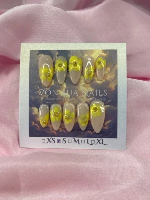 ButterBloom (S);Medium Almond - Handgjorda press-on naglar i storlek S: 15 mm, 11,5 mm, 12 mm, 11 mm, 9 mm . Naglarna har en nude bas med gula blommor och små guldfärgade detaljer. Formen är almond och medium längd. Perfekt för dig som vill ha en unik och färgglad nageldesign.