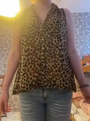 Leopardmönstrad ärmlös blus - Säljer en ärmlös blus med leopardmönster. Toppen har krage och knäppning framtill, samt en lös och luftig passform. Perfekt för dig som vill sticka ut med ett djurmönster i garderoben.