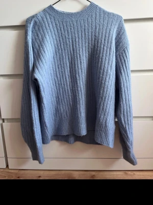 Ljusblå ribbstickad tröja H&M - Mysig ljusblå stickad tröja från H&M i ribbstickat material. Tröjan har rund halsringning, långa ärmar och en avslappnad passform. Perfekt för kyliga dagar och enkel att matcha med jeans eller kjol.