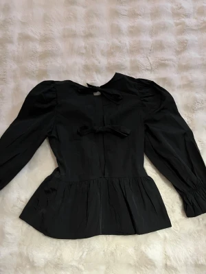 Svart blus med puffärm och rosetter - Trendig svart blus med puffiga armar och två rosetter på ryggen. Rosetterna går att knyta💕 storlek xs och kommer från Hm.