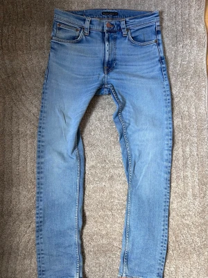 Ljusblå jeans från Nudie Jeans -  Hej och välkomna till Liljestrands Nu säljer vi ett par jeans från nudie Som är i mycket bra skick endast lite slitet vi skrevet Som syns i bild två Storlek 29 / 30. Det är modellen lean Dean Kom med frågor och så vidare så hörs vi. MVH Liljestrand