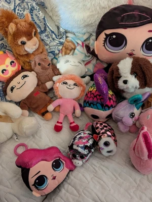 Blandade gosedjur och mjukisdjur - Samling med olika gosedjur och mjukisdjur i flera färger och former, bland annat hund, ekorre, enhörning, kanin, samt dockor och figurer med stora ögon. Materialet är mjuk plysch och tyg, vissa med broderade detaljer och färgglada mönster.