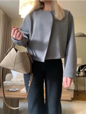 Snygg grå kort jacka  - Snygg grå kort jacka i stilren och minimalistisk design. Perfekt till både vardag och mer uppklädda outfits. Den har en modern, något oversized passform utan knappar framtill vilket ger en väldigt elegant look🤍 Storlek M
