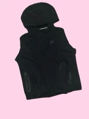 Svart Nike tech med huva - Snygg svart Nike tech från Nike med huva och hel dragkedja framtill. Flisjackan har två fickor med dragkedja och en diskret Nike-logga på bröstet. Perfekt för lager-på-lager och sportiga outfits.