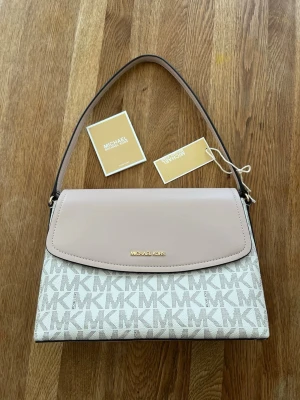 Michael Kors vit och rosa handväska - Jättefin rosa/vit mönstrad Michael Kors väska med prislapp kvar. Kommer med ”care card” och ett längre rosa axelband som tillhör väskan. Måtten är ungefär 20 cm x 30 cm x 10 cm. Nypris på den här varianten är ungefär 3500-4000kr men finns inte att köpa längre. Säljer för 2500 nu. Kan diskutera priset! 🩷