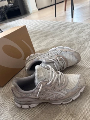 Asics GEL NYC - Snygga sneakers från ASICS i beige och grå toner. Skorna har en kombination av mesh och mockadetaljer, samt klassisk ASICS-logga på sidan.  Storlek 44,5