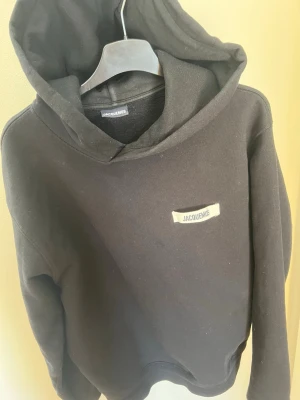 Svart hoodie från Jacquemus - Snygg svart hoodie från Jacquemus med minimalistisk design och liten vit logotyp på bröstet. Klassisk passform med stor huva och ribbade muddar. Perfekt för dig som gillar stilrena plagg med streetkänsla. Använd ett fåtal gånger, tvättar den innan jag skickar!