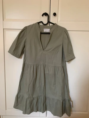 Ljusgrön kortklänning från ASOS DESIGN - Supersnygg ljusgrön kortklänning från ASOS DESIGN med v-ringning och volangdetalj nedtill. Klänningen har halvkort ärm och en avslappnad passform som ger en chill vibe. Perfekt för varma dagar och enkel att styla med sneakers eller sandaler.