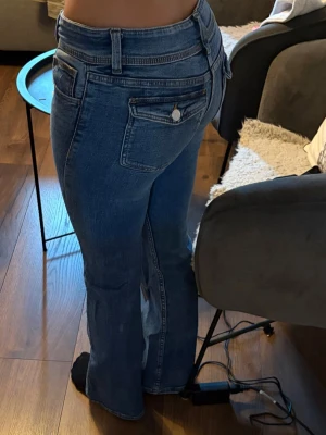 Blå bootcut jeans med fickdetaljer - blå bootcut jeans med klassiska fem fickor och extra ficklock bak. Jeansen har låg midja, dubbla knappar och är stretchiga tycker jag.
