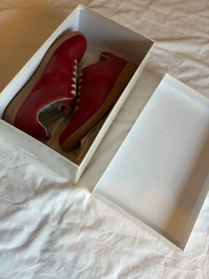 Maison Margiela Gats - Snygga röda sneakers med vita snören och beige sula. Skorna har en mix av mocka och läderdetaljer som ger en cool och sportig vibe. Perfekta för dig som vill sticka ut med färg på fötterna. Klassisk låg modell som funkar till många stilar.