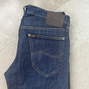 Mörkblå jeans från Lee - Snygga mörkblå jeans från Lee med klassisk femficksdesign och Lee-logga på bakfickan. Jeansen har normal passform och är tillverkade i slitstarkt bomullsjeansmaterial. Perfekta för dig som gillar en tidlös och stilren look. W29 L32