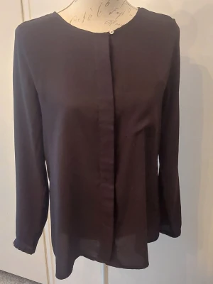 Svart långärmad blus med dold knäppning - Stilren svart blus med rund halsringning och dold knäppning framtill. Långärmad modell i ett lätt och något transparent tyg som ger en luftig känsla. 