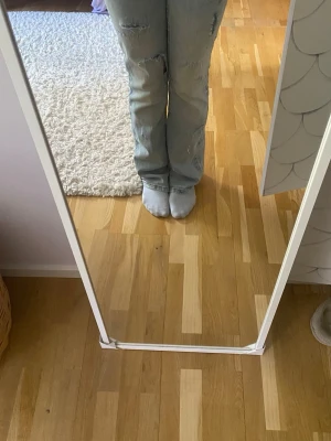 Ljusblå bootcut jeans med slitningar - Säljer ett par ljusblå bootcut jeans med snygga slitningar på benen. Jeansen har klassisk femficksdesign och är tillverkade i denim. Perfekta för dig som gillar en avslappnad och trendig stil. Lite långa i benen på mig som är 162cm! Skriv för fler bilder eller frågor