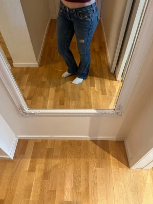 Blå bootcut true religion jeans  - Snygga blå bootcut jeans. Jeansen har låg midja och detaljerade sömmar vid fickorna. Perfekta för en avslappnad och trendig look. Inte mycket använda och jag är 164 cm lång. Storlek 26 
