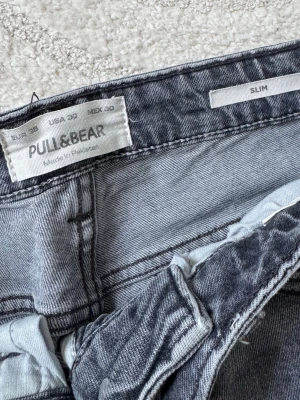 Grå slim jeans från Pull&Bear - Snygga grå slim fit jeans från Pull&Bear med klassisk femficksdesign och dragkedjegylf. Jeansen har en tvättad look och raka ben, perfekta för en avslappnad stil. 