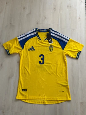 Sverige tröja - Gul och blå Sverige fotbollströja från Adidas med Lindelöf och nummer 3 på ryggen. Tröjan har korta ärmar, blå detaljer på axlar och ärmslut samt det svenska landslagets emblem på bröstet. Tillverkad i lätt och ventilerande material.