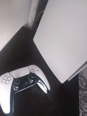 PlayStation 5 med DualSense-kontroll - PlayStation 5 konsol i vit och svart med tillhörande DualSense-kontroll. Snygg futuristisk design med rundade kanter och matta paneler. Perfekt för gaming och upplevelser i toppklass.