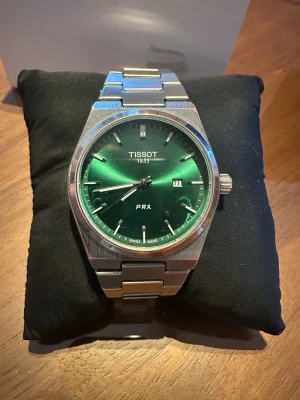 Tossot prx green dail/ silver case - Klockan kommer med originalbox, påse, extra länkbitar samt verktyg för justering av länken. Perfekt både till vardag och mer uppklädda tillfällen. Lite repor här och där och lite oxsidering vid bezeln. Den gröna tavlan skiftar snyggt i ljuset och ger klockan ett exklusivt uttryck. NYPRIS 4000KR  📦 Ingår: • Originalbox • Tissot-påse • Extra länkbitar • Verktyg för länkjustering 