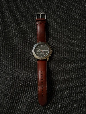 Michael Kors klocka med brunt läderband - Stilren klocka från Michael Kors med svart urtavla, silverfärgat boett och brunt läderband. Klockan har kronograf-funktion och tydliga markeringar på urtavlan. Perfekt accessoar för dig som gillar klassisk men modern stil. (Klockan behöver byta batteri).