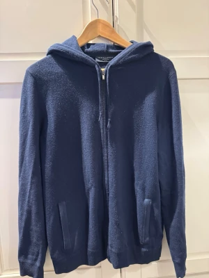Mörkblå hoodie med dragkedja - Mörkblå hoodie från Charles Tyrwhitt med dragkedja framtill och två fickor. Tillverkad av bomull och kashmir och har en klassisk huva. Perfekt för en avslappnad och stilren look.