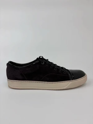 Svarta Lanvin sneakers med lackad tå - Snygga svarta sneakers med ovandel i mocka och glansig lackad tå. Skorna har svarta skosnören och en vit sula som ger en clean kontrast. Perfekta för dig som gillar en stilren men ändå unik look.
