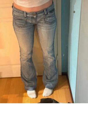 Ljusblå bootcut jeans från Only - Säljer ett par ljusblå bootcut jeans från Only med klassiska fem fickor och snygga slitningar. Jeansen har låg midja och utsvängda ben, samt detaljerade sömmar och logga på bakfickan. Perfekta för en avslappnad och trendig look.