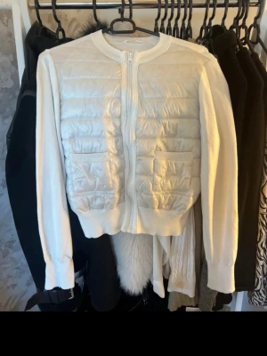 Vit quiltad cardigan med dragkedja - Snygg vit cardiganjacka med quiltad framsida och två fickor. Jackan har dragkedja framtill, rund halsringning och långa ärmar i mjukt material. Perfekt för lager-på-lager och en clean look.