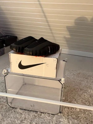 Svarta Nike MMW 005 tofflor - Säljer ett par svarta Nike Mind tofflor i storlek 43. Helt oanvända och i nyskick – lapparna sitter fortfarande kvar och originalboxen medföljer.  Otroligt sköna och stilrena tofflor som passar perfekt både hemma, efter träning eller till vardags. En enkel men modern design som funkar till det mesta.  Storlek: 43 Färg: Svart Skick: Oanvända, med tags och box kvar Pris: 1199 kr