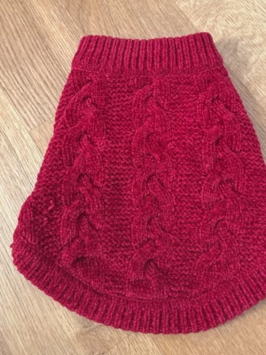 Vinröd stickad hundtröja - Mysig vinröd stickad hundtröja med flätmönster och ribbade kanter. Tröjan har öppningar för frambenen och är perfekt för att hålla din hund varm under kyliga dagar. Tillverkad i mjukt garn för extra komfort.