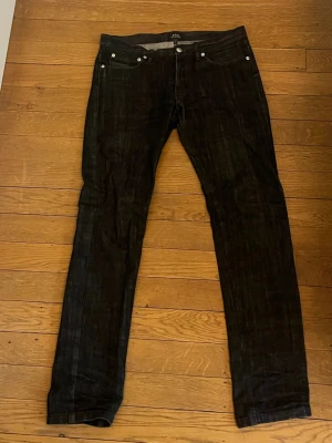 A.P.C. Jeans - Snygga svarta jeans från A.P.C. med klassisk femficksdesign och raka ben. Modellen är Petite Standard och kostar ca 2100kr nypris. Tyvärr så har jeansen en liten defekt som finns på sista bilden men det syns inte med jeansen på! Priset är inte hugget i sten