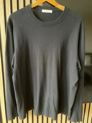 Svart stickad tröja Paul & friends - Klassisk svart merinoull tröja från Paul & friends med rund halsringning och ribbade muddar. Enkel och stilren design som passar till det mesta. Perfekt basplagg för garderoben.