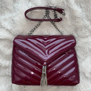 Vinröd väska - lackad  - Hej hej, säljer en fin liten vinröd väska i ett lackat material. Den är köpt här på Plick för nåt år sen men har aldrig kommit till användning!! Säljaren innan mig har förkortat väskan men det är något man kan ta bort ifall man önskar längre band! (Sitter med tejp på insidan) OBS! Köparen står för frakten💋🍸