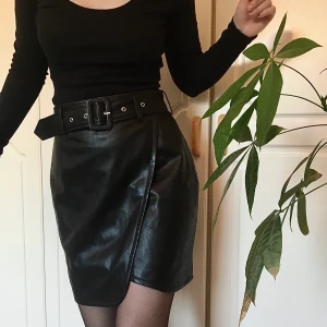 Kjol i svart skinnimitation från NA-KD - Svart kjol i skinnimation som är i precis lagom längd - ca 48 cm, med en midja på 70 cm. Storlek är 36 men passar nog även 38 då den är lite större i storleken. Vacker slits framtill som framhäver benen. Säljs i nyskick, endast provat ett fåtal gånger. Matchande skärp medföljer!