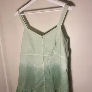 Ett linne med spetsdetaljer i en grön färg som går från ljust till mörkt och har knappar på framsidan. 