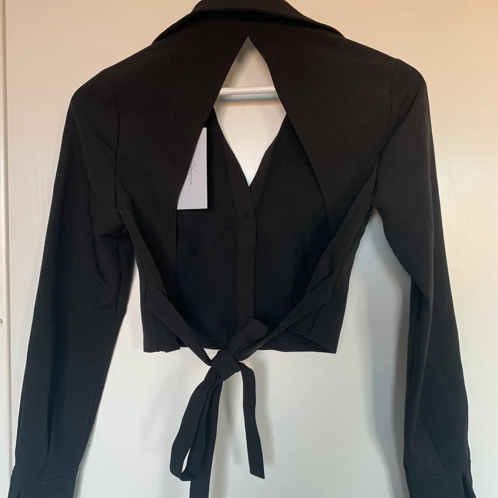 Jättesnygg svart croppad skjorta med öppen rygg ifrån na-kd x Hanna Schönbergs kollektion! Den är i storlek 32, jag har vanligtvis 34 och den passar mig men har tyvärr inte kommit till användning❣️ prislappen sitter kvar. Säljer den för 100kr🥰. Skjortor.