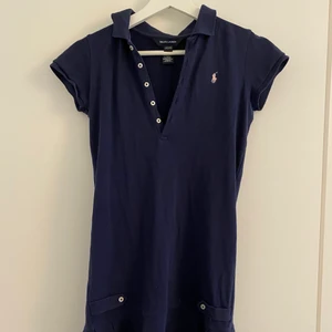 Ralph lauren klänning - Så fin mörkblå Ralph Laurent klänning som har ett rosa märke. Den sitter så fint på men den är inte min stil längre. Tyget är väldigt bra kvalitet och klänningen är som ny! ❤️❤️❤️