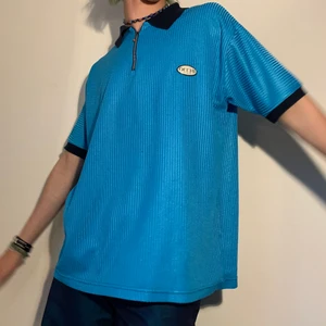 Turkos vintage oversized half zip krage - Turkos vintage oversized half zip kortärmad tröja med mörkblå krage och kanter 👕 Alla detaljer på denna tröjan, att dragkedjan har en ball chain, det coola glansiga tyget och den balla svartvita loggan som säger ”OCCHI” i asballt reflex material, gör denna tröjan så unik men ändå så casual! Den är så snygg till ett par mörka jeans för att matcha det mörkblåa i tröjan eller bara ett par svarta kostymbyxor för att matcha den svarta texten i loggan! Sedan ett par ljusa sneakers så är du good to go!
