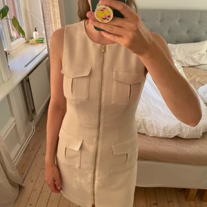 Klänning strl 38 - Fin fodralklänning från HM i strl 38. Beige, ”safaribeige”. Fint blixtlås i guld som går längs hela klänningen, ger smickrande intryck. Använd ytterst sparsamt, kanske 2 gånger max.