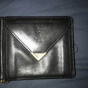 VINTAGE Yves saint Laurent plånbok (äkta såklart) med sedelklämma och detaljer i guld.förutom sedelklämman så har du myntfack och 3 fack för kort. Svart läder. Begagnad men mycket välbehållen.