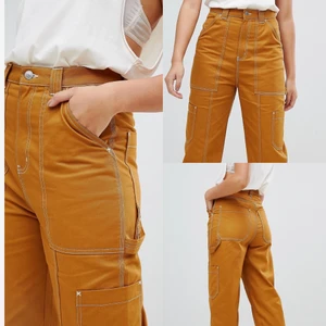 Orange street byxa - Orange/brun högmidjad (över naveln) byxa från Weekday med vita detaljer. Cool streetwear design med fickor i sidan.   Storlek 36. True to size.   OBS: Dragkedja lossnat från fäste så kan inte knäppas. Går troligen att laga, men därav nersänkt pris! (Se sista bild) Nypris: ca 500 kr Mitt pris: 100 kr inkl frakt