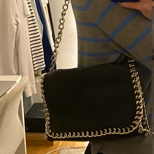 Svart väska - En jättefin väska från Scorett med märket Tiamo. Väskan är tänkt att ha som på bild 2 men jag har satt dit en nyckelring (bild 3) som gör att man själv kan välja hur lång den ska vara, exempelvis som på bild 1! Skicka privat vid frågor eller för fler bilder💕  Bredd: Ca 26 cm Höjd: Ca 18-19 cm Bredd i botten: Ca 6 cm