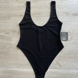 Body - Snygg oanvänd body i ribbat tyg från Nelly.com med djup rygg och string modell. Helt ny med lapparna kvar, storlek S,