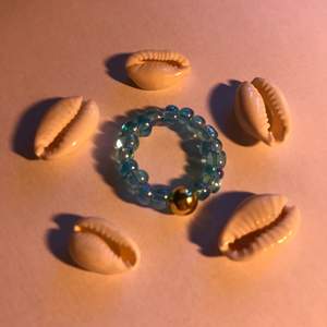 Ring med små blå genomskinliga pärlor, en rund guld pärla och elastisk tråd! Runt 6 cm! 15kr plus frakt!