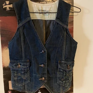 Väst från Wrangler - Jeansväst från Wrangler Hittar ingen storleksmärking, se mått. Längd: 50 cm Bredd: 40 cm 100% bomull Uppskattar storleken till S-M