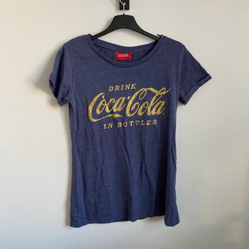 Blå, spräcklig T-shirt med Coca Cola logga på. . T-shirts.