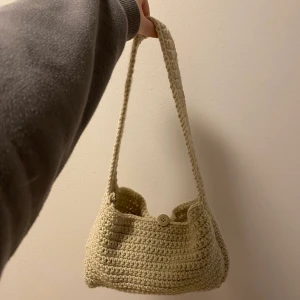 Virkad baguetteväska beige - Virkad beige baguetteväska (gjord av mig). 100% akryl. Längden är ca 26-27cm, höjden ca 15 cm och djupet ca 3-4 cm. Axelbandet är ca 60 cm långt. Axelbandet sitter lite snett på de båda sidorna, men syns knappt vid användning (pratar om ca 1-2 cm snett). Knappen går att knäppa upp💫💫120kr inkl frakt med frimärken