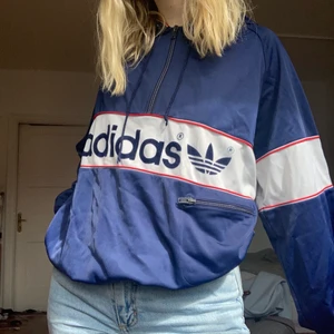 Vintage Adidas hoodie - Säljer en vintage adidashoodie i blått med röda och vita detalje i riktigt fint skick! Går att öppna och stänga med dragkedja till bröstet. På vänster sida finns en ficka som även den stängs med dragkedja. Trycket är gjort i sammet. Jag har storlek S så passar en S-M men kan ge exakta mått om så önskas. En riktigt pärla men kommer tyvärr aldrig till användning hos mig. Säljes för 250 kr + 66 riksdaler frakt. Hojta om du vill se fler bilder!💙