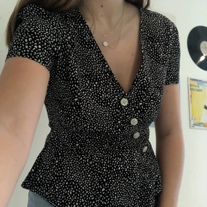 Prickig kortärmad blus i strl XS - Svart kortärmad blus med vita prickar. Blusen har knappar och går in en aning i midjan, vilket gör att den framhärver kurvor. Luftigt material. Köparen står för frakt. 